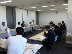 長方形に並べられ、資料が置かれた机の周りに座る男性たちの写真