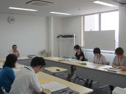 長方形に並べられた机の前の椅子に座りながら資料を眺める人々の写真