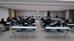 4列に並べられた長机に2人ずつ座っている参加者達を会議室の後方から写した写真