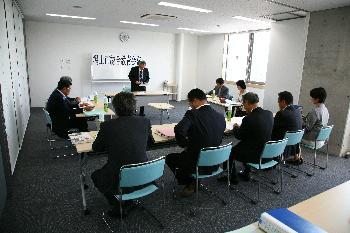 会議室のホワイトボードの前で議会を進行する市長とテーブルに座って聞いている構成員たちの写真