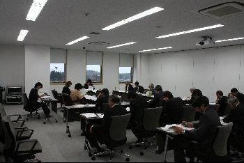 会議室で会議を開いている人たちとその様子を聞いている人たちの写真