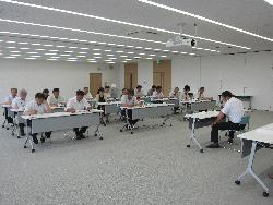 大会議室でYシャツ姿で会議をしている参加者たちの様子の写真