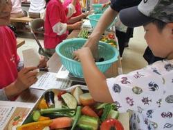 野菜の重さ当てゲームのコーナーで量りの上の籠の中に参加者親子が野菜を入れている写真