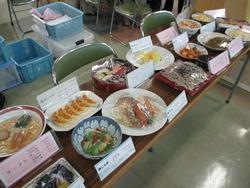 テーブルの上にラーメン、餃子、すし、そばなどの料理が展示されている写真