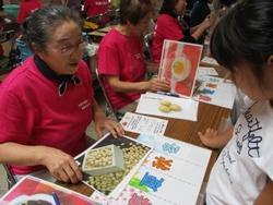 升に入った大豆の資料を女性スタッフが机の上で掲示し、参加者が食べられる季節を考えている写真
