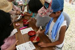 割り箸を持って豆つかみに挑戦する男の子や女の子の写真